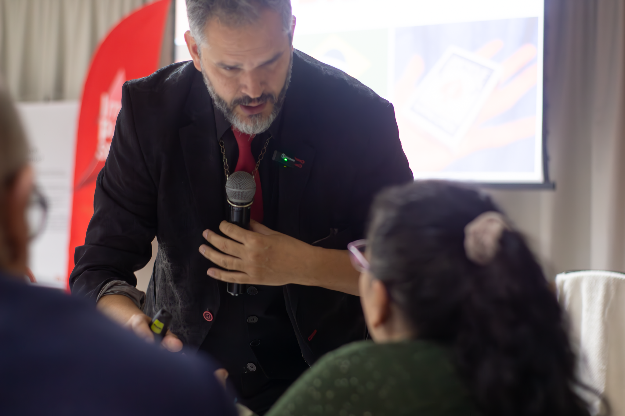 Palestrante interage com participante em evento corporativo, segurando microfone e apontando com energia.
