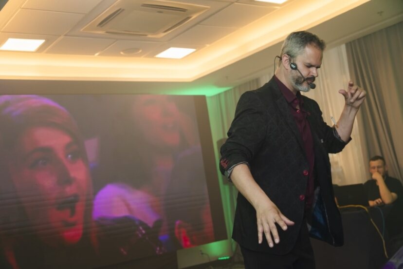 Mágico Paul & Jack se apresentando em um casamento, com expressão concentrada, microfone de cabeça e plateia ao fundo reagindo com surpresa e encantamento.