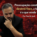 Homem pensativo em primeiro plano, com expressão de preocupação e mão no rosto, enquanto um público ao fundo aparece desfocado e em tom avermelhado, ilustrando a tensão entre distração externa e foco mental no ambiente de negócios.