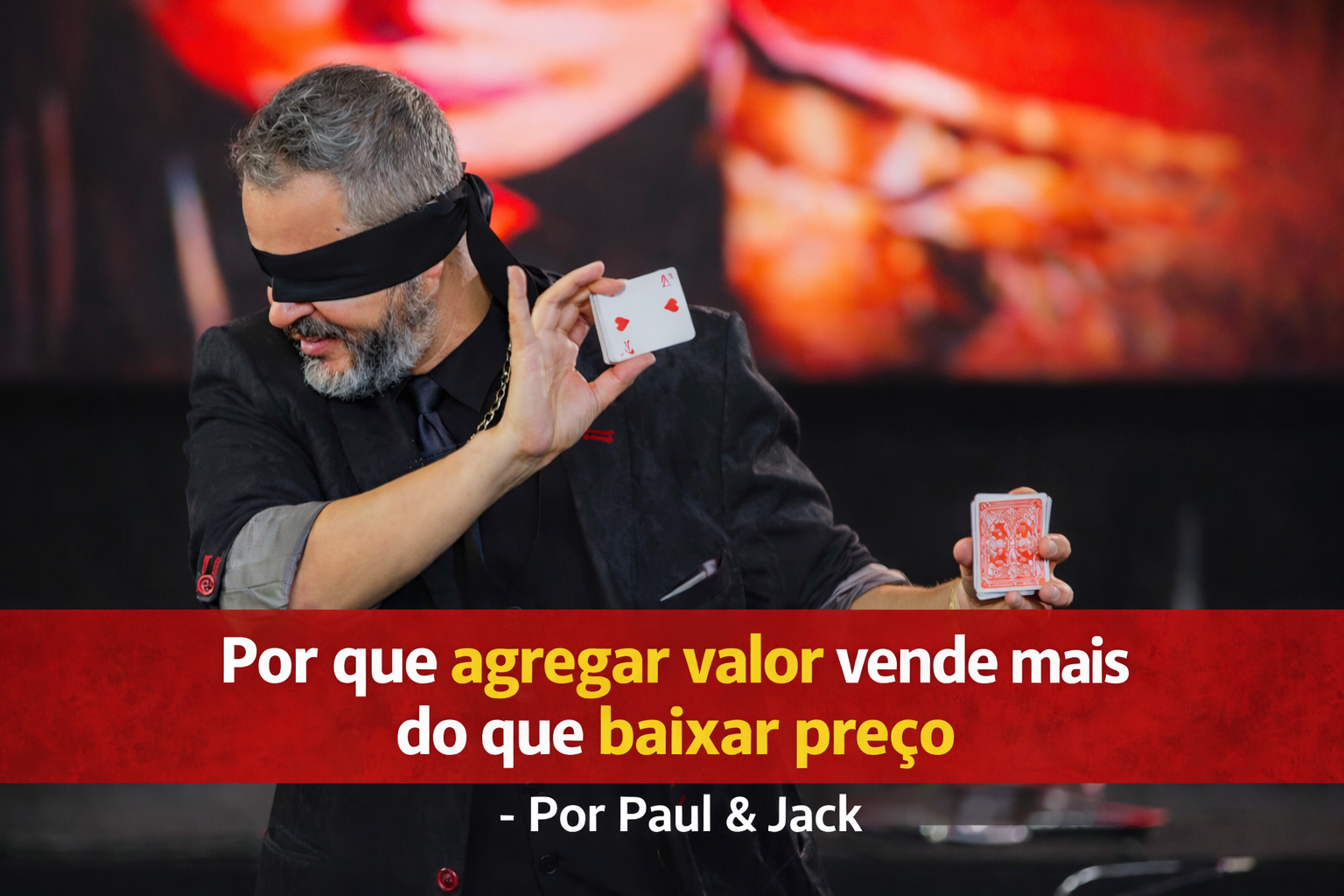 Palestrante realizando demonstração com cartas de baralho, vendado, em palco, usando terno escuro, com faixa vermelha destacando o título sobre valor e preço ao fundo.