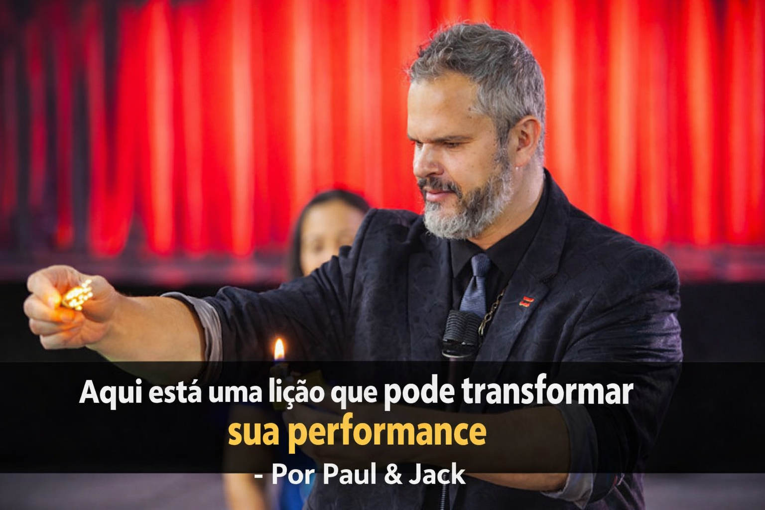 Homem palestrante em palco, segurando uma chama acesa durante demonstração ao vivo, com expressão concentrada, fundo iluminado em vermelho e título em faixa preta sobre a imagem.