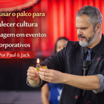 Palestrante realizando truque com fogo no palco durante evento corporativo, com o título “Como usar o palco para fortalecer cultura e mensagem em eventos corporativos – Por Paul & Jack”.
