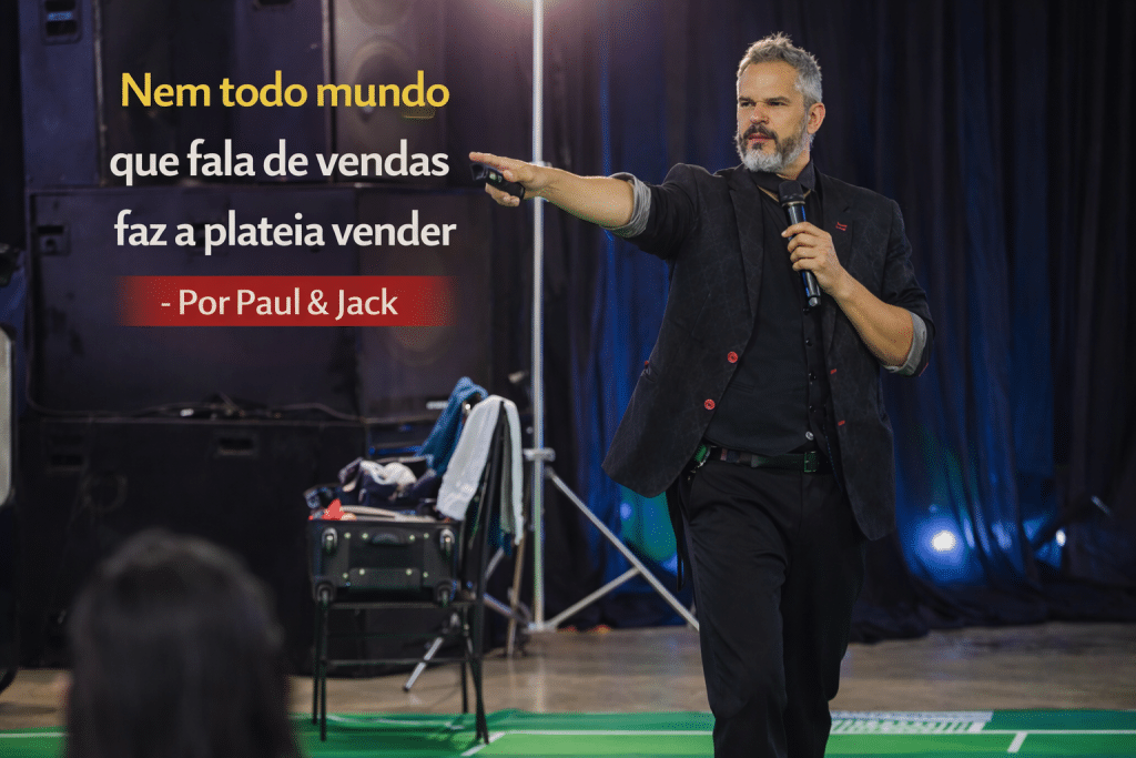 Palestrante em palco apontando para a plateia durante evento corporativo, com o título “Nem todo mundo que fala de vendas faz a plateia vender – Por Paul & Jack”.