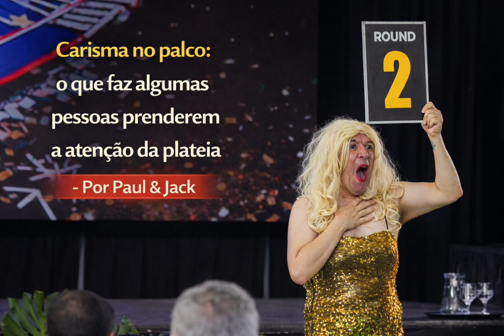 Apresentador no palco com vestido dourado segurando placa “Round 2”, com o título “Carisma no palco: o que faz algumas pessoas prenderem a atenção da plateia – Por Paul & Jack”.