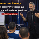 Palestrante em pé diante da plateia durante evento corporativo, gesticulando com as mãos e microfone, com o título “Palestra para liderança: como desenvolver líderes que comunicam, influenciam e mobilizam – Por Paul & Jack”.