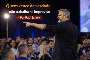 Palestrante de perfil, apontando para a plateia durante apresentação corporativa, com o título “Quem vence de verdade não trabalha no improviso – Por Paul & Jack”.